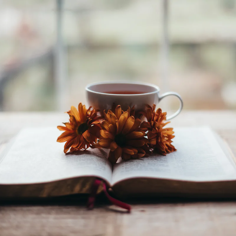 An open book with a cup of tea and orange flowers on a wooden table